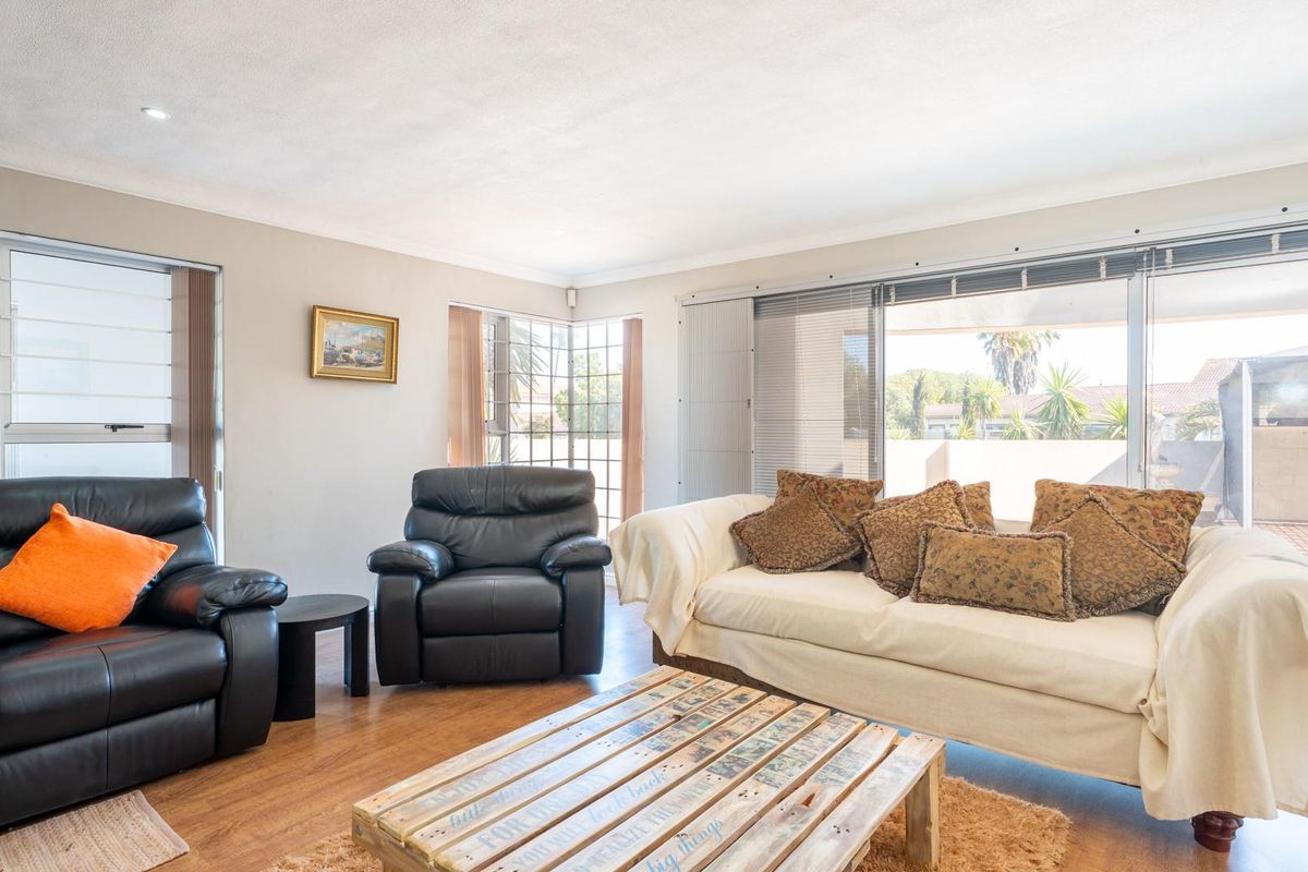A bright and spacious living room featuring laminate flooring, large windows, and sliding glass doors that provide access to the outdoor patio area.