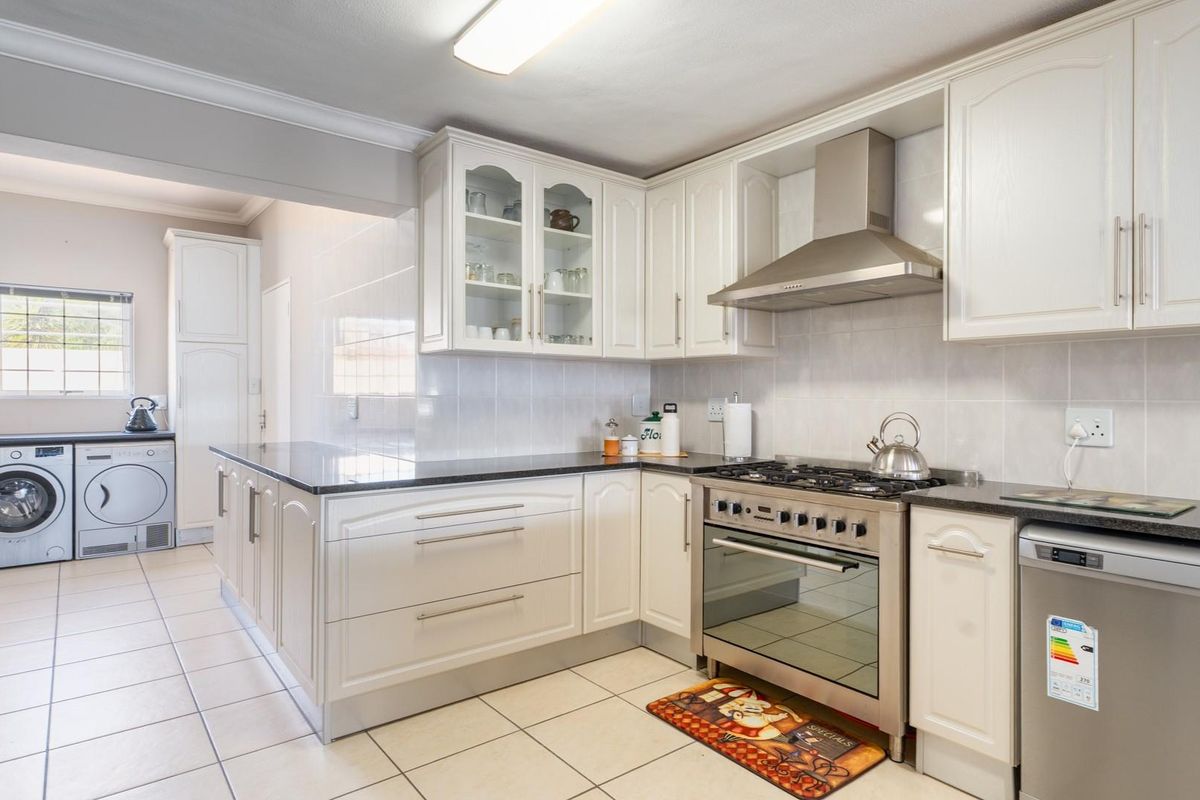 A functional kitchen featuring white cabinetry, dark countertops, a stainless steel gas stove with extractor fan, and a dedicated laundry area with tiled flooring.