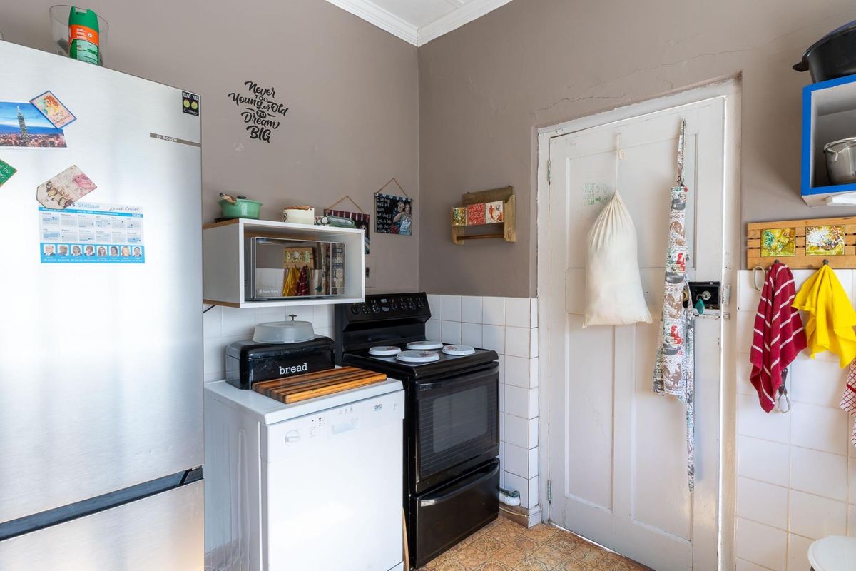 A compact kitchen area featuring a freestanding stove, tiled splashback, and vinyl flooring, with a traditional wooden door leading to an adjacent space.