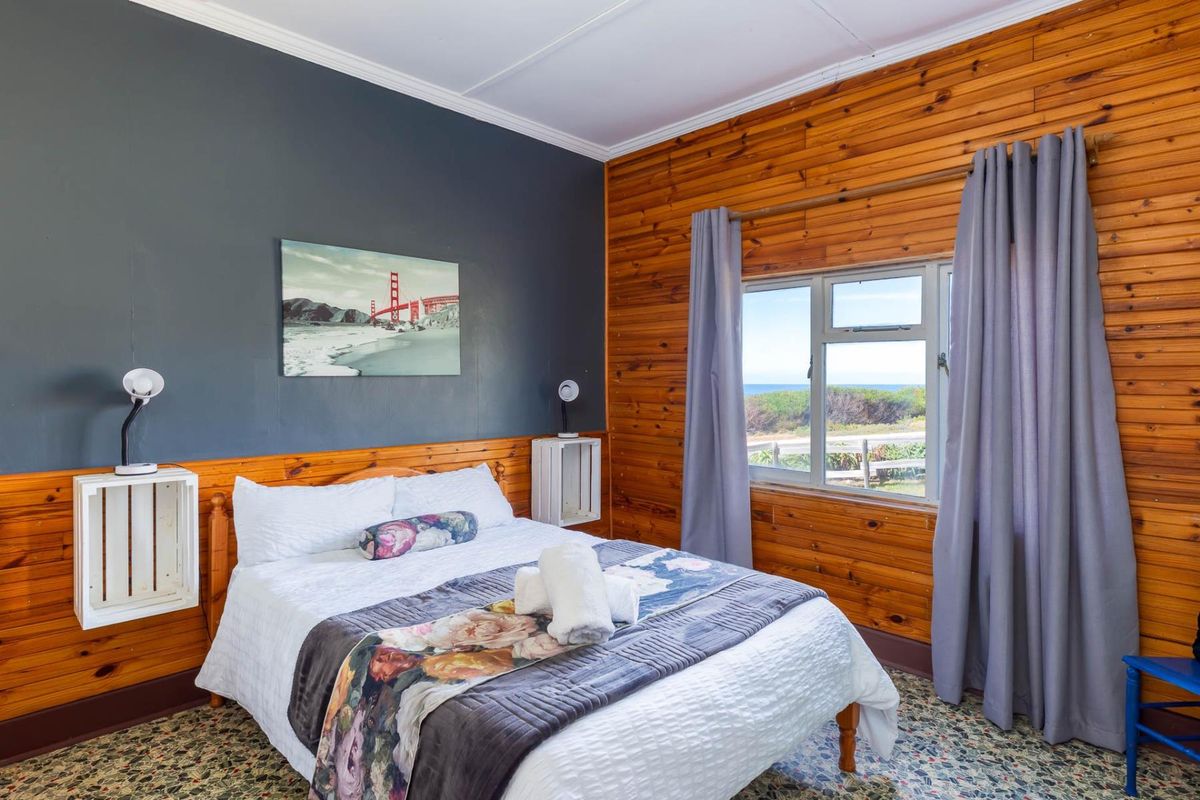 A bedroom featuring a mix of dark painted walls and natural wood paneling, with a window offering coastal views.