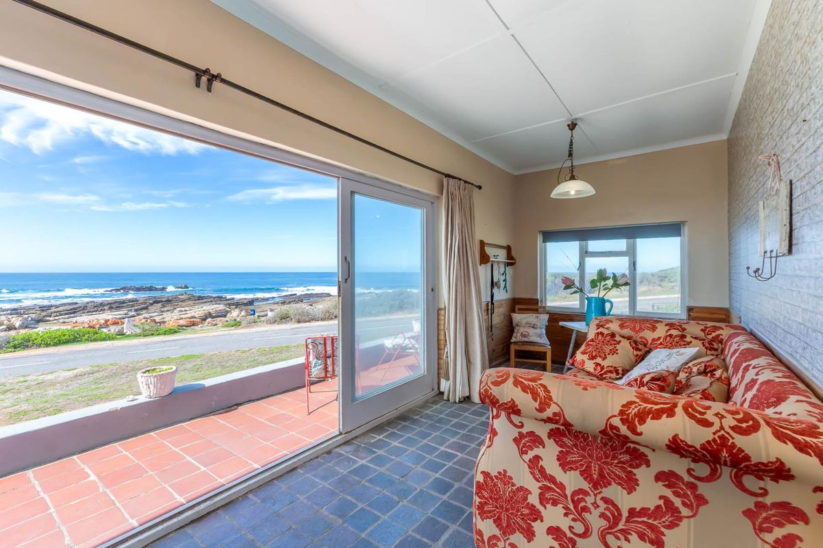 A sunlit living area featuring large sliding glass doors that open onto a tiled patio with expansive ocean views.