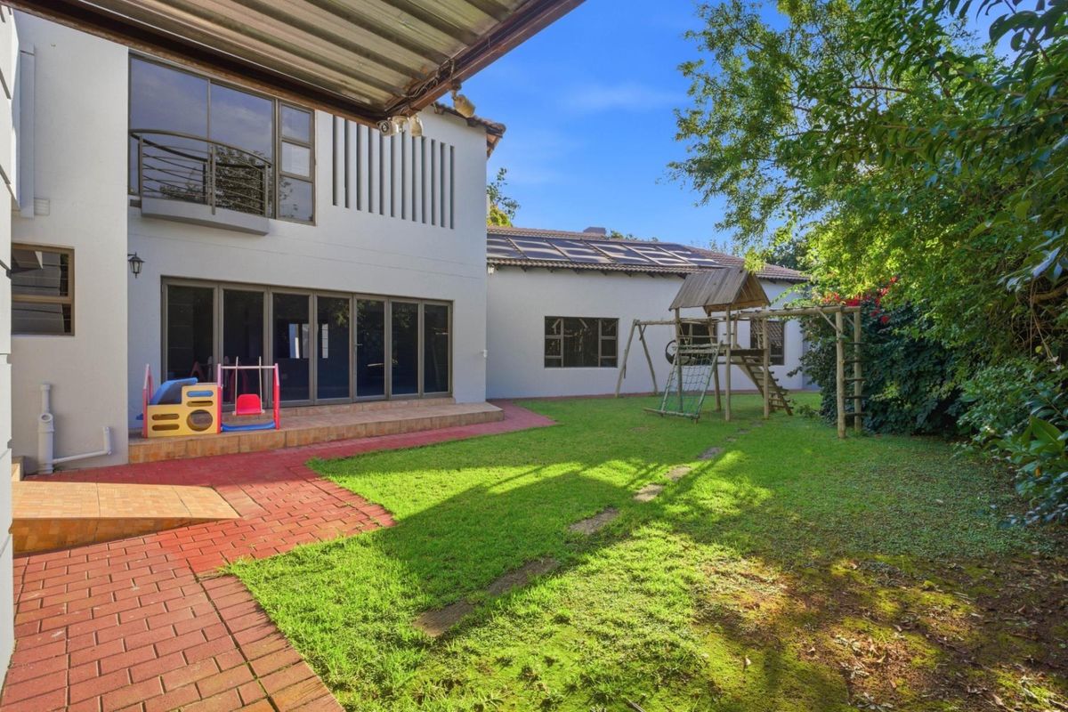 A spacious rear garden featuring a paved patio area, lush lawn, and a multi-level exterior facade with large glass sliding doors.