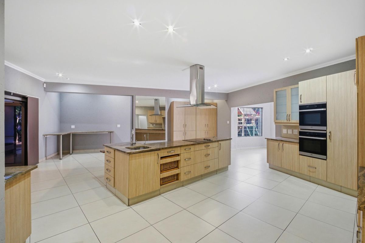 Spacious modern kitchen featuring light wood cabinetry, a central island with integrated sink and hob, and built-in double ovens.