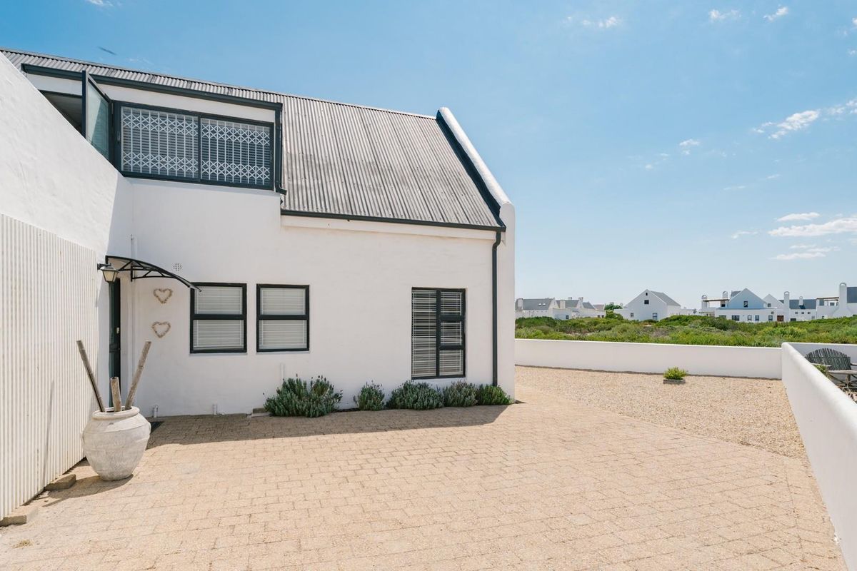 A well-maintained exterior rear view featuring a paved patio area, white rendered walls, and a corrugated metal roof.