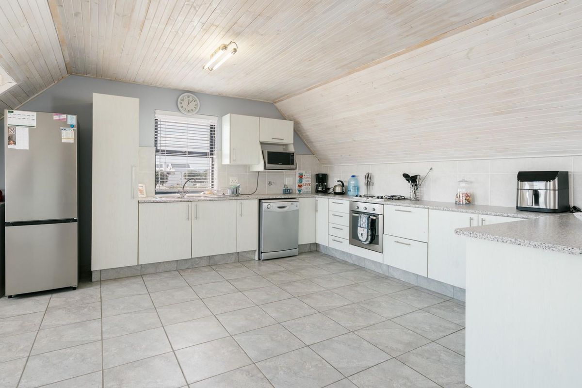 A functional kitchen featuring white cabinetry, granite-style countertops, tiled flooring, and a vaulted timber-clad ceiling in an attic-style space.