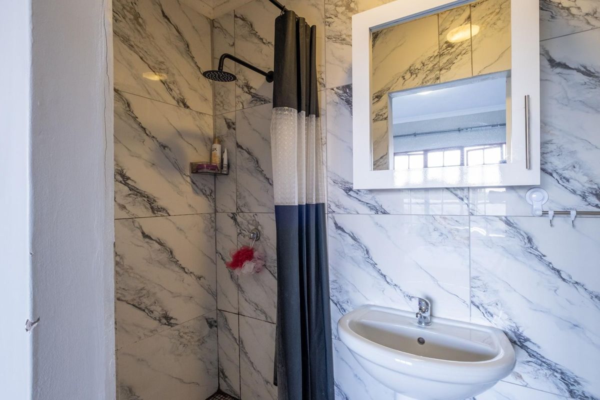 A modern bathroom featuring marble-look wall tiles, a pedestal basin, a wall-mounted mirror cabinet, and a walk-in shower with a rainfall showerhead.