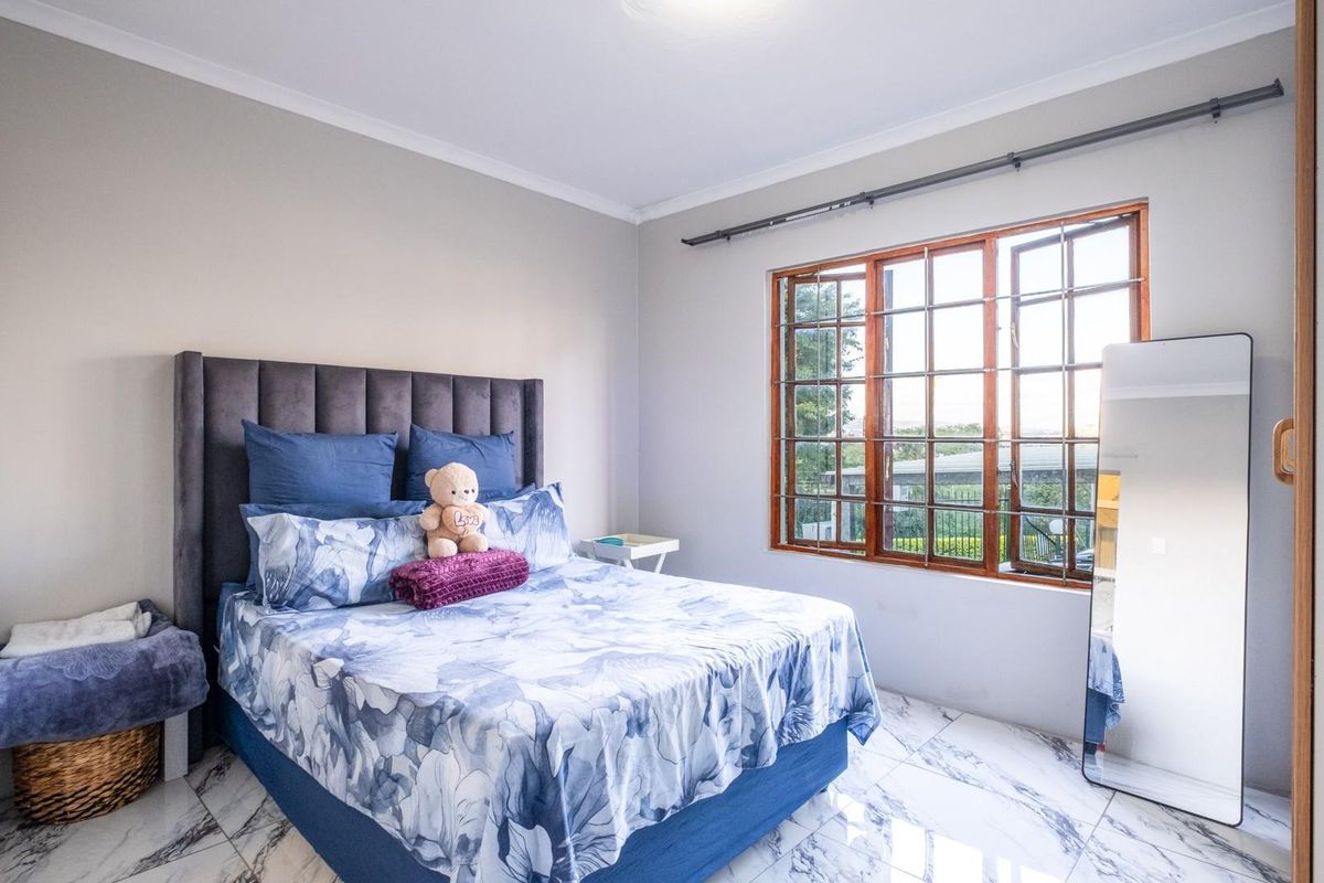 A bright bedroom featuring marble-look tiled flooring, a large window with security bars, and neutral wall finishes.