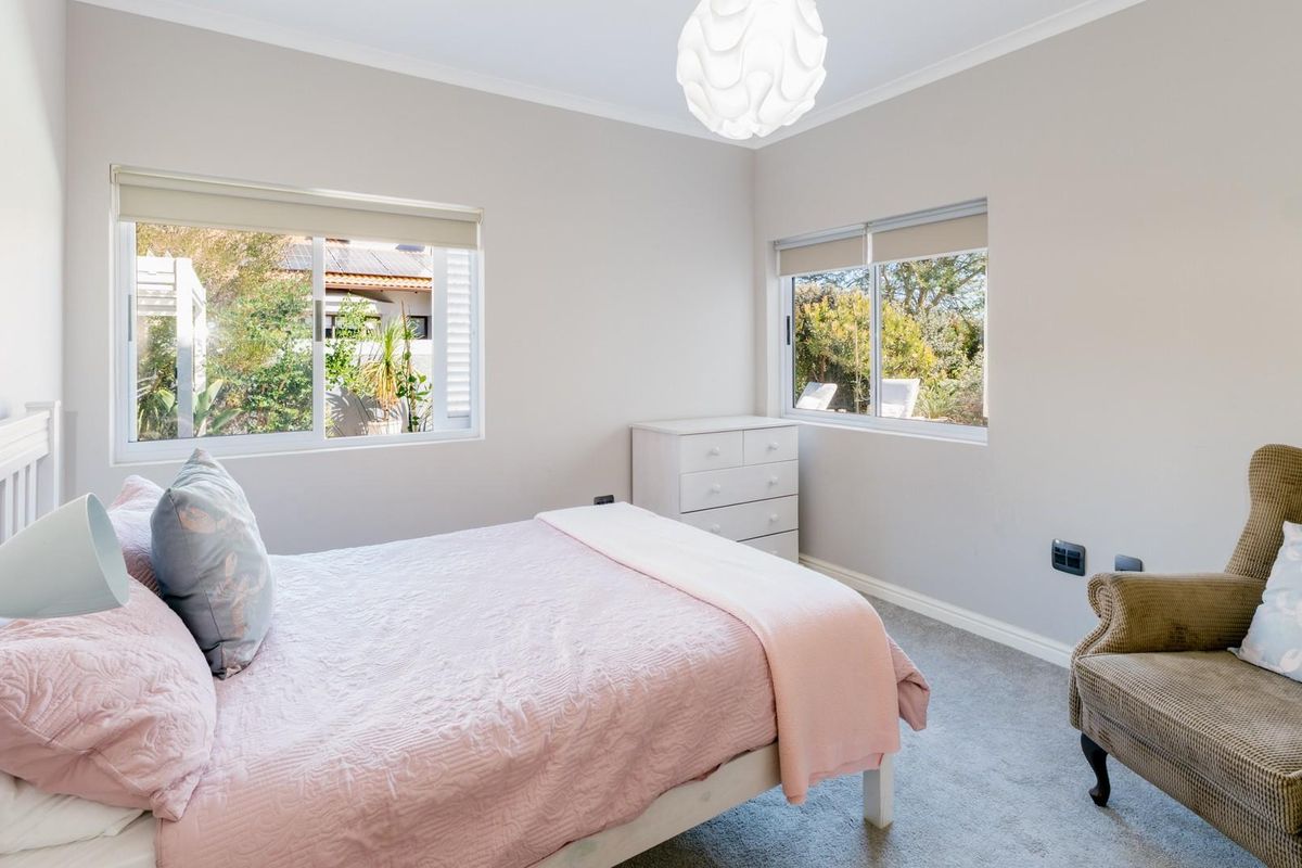 A bright and well-maintained bedroom featuring neutral wall tones, plush carpeting, and large windows that provide ample natural light and garden views.
