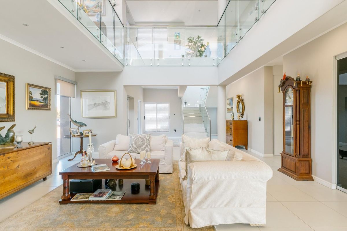 Spacious double-volume living area featuring a glass balustrade mezzanine, tiled flooring, and an open-plan layout with a staircase leading to the upper level.