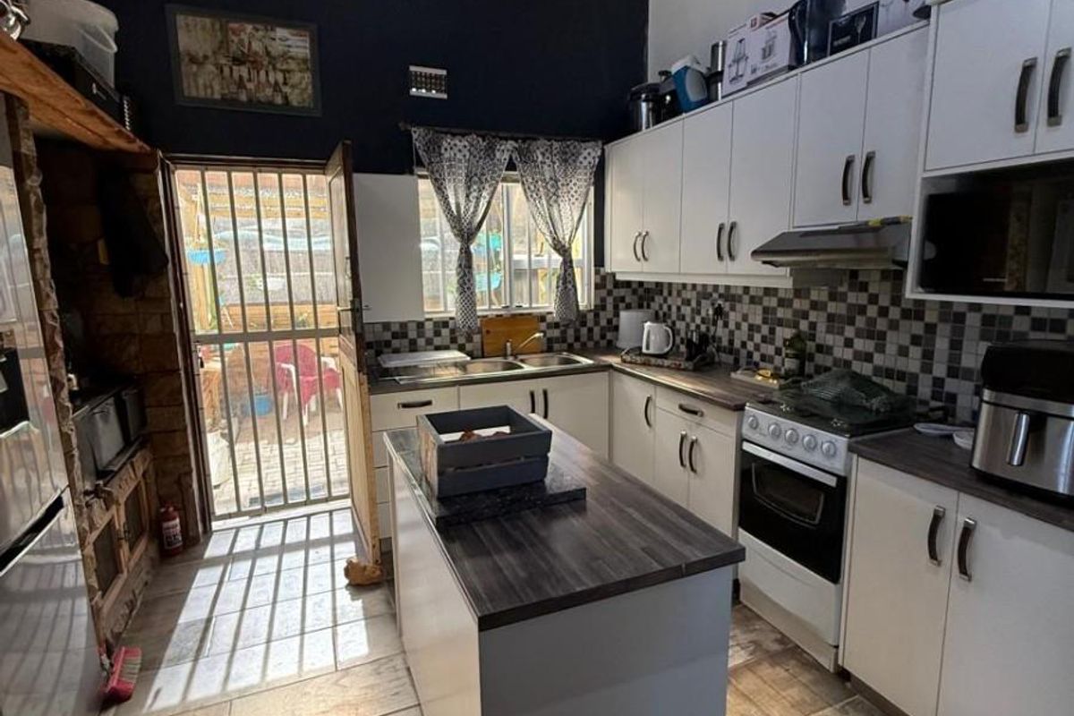 A functional kitchen featuring white cabinetry, a central island, tiled backsplash, and a high timber-paneled ceiling with direct access to the rear exterior.