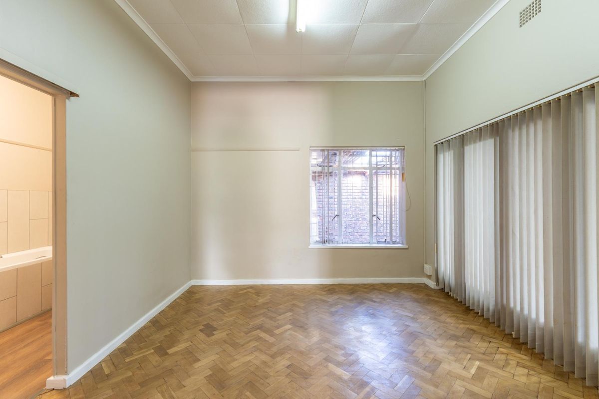 A spacious, empty bedroom featuring classic parquet flooring, vertical blinds, and direct access to an adjoining bathroom.