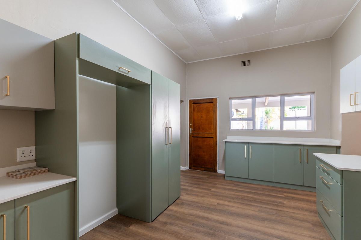 A functional kitchen featuring sage green cabinetry, white countertops, wood-look flooring, and a solid timber door leading to the exterior.