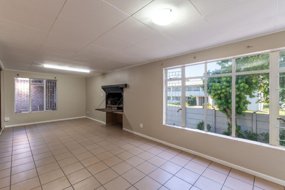 Spacious living area featuring tiled flooring, large windows for natural light, and a built-in indoor braai fireplace.