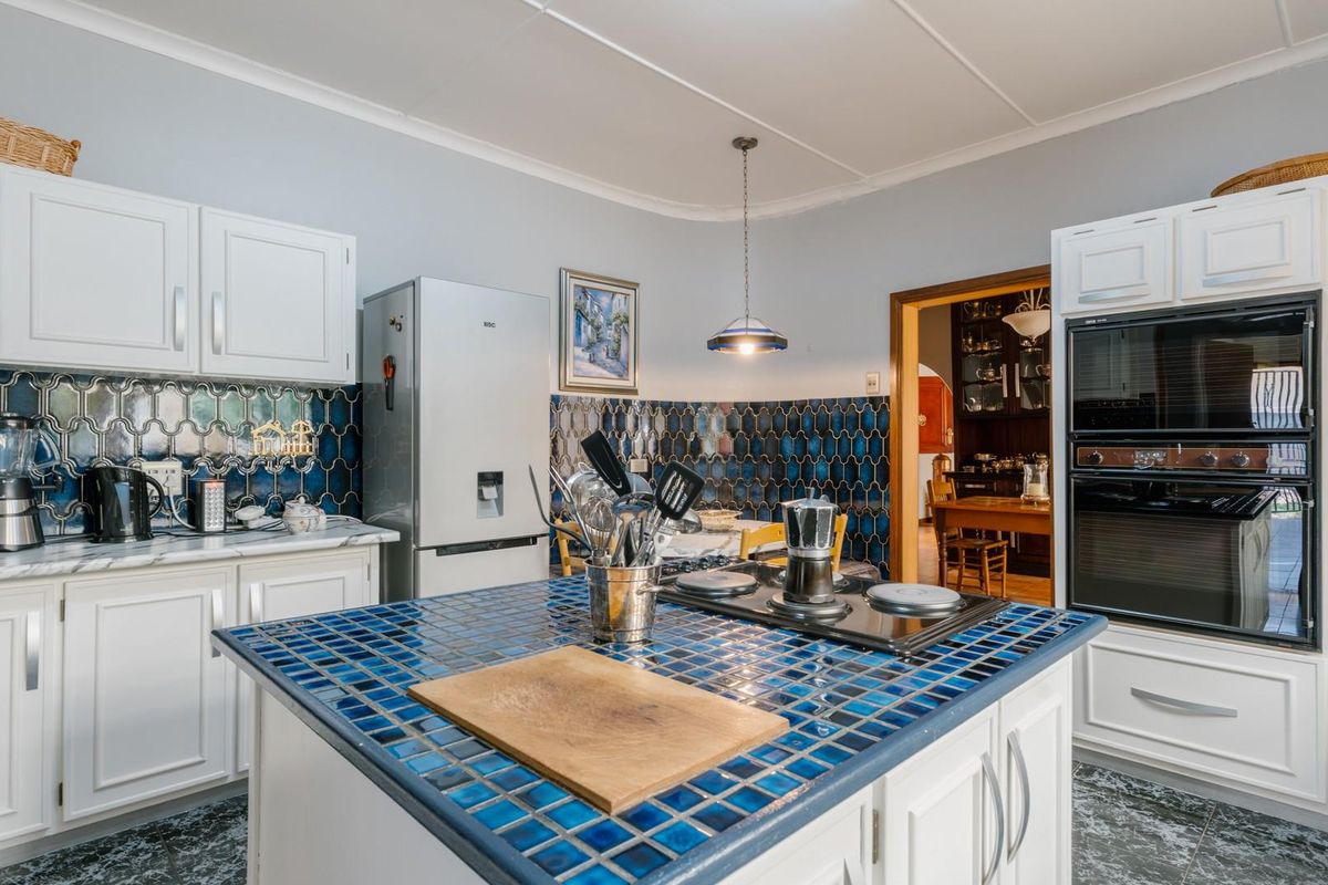 A functional kitchen featuring a central island with a tiled countertop, built-in oven, and distinctive blue decorative wall tiling.