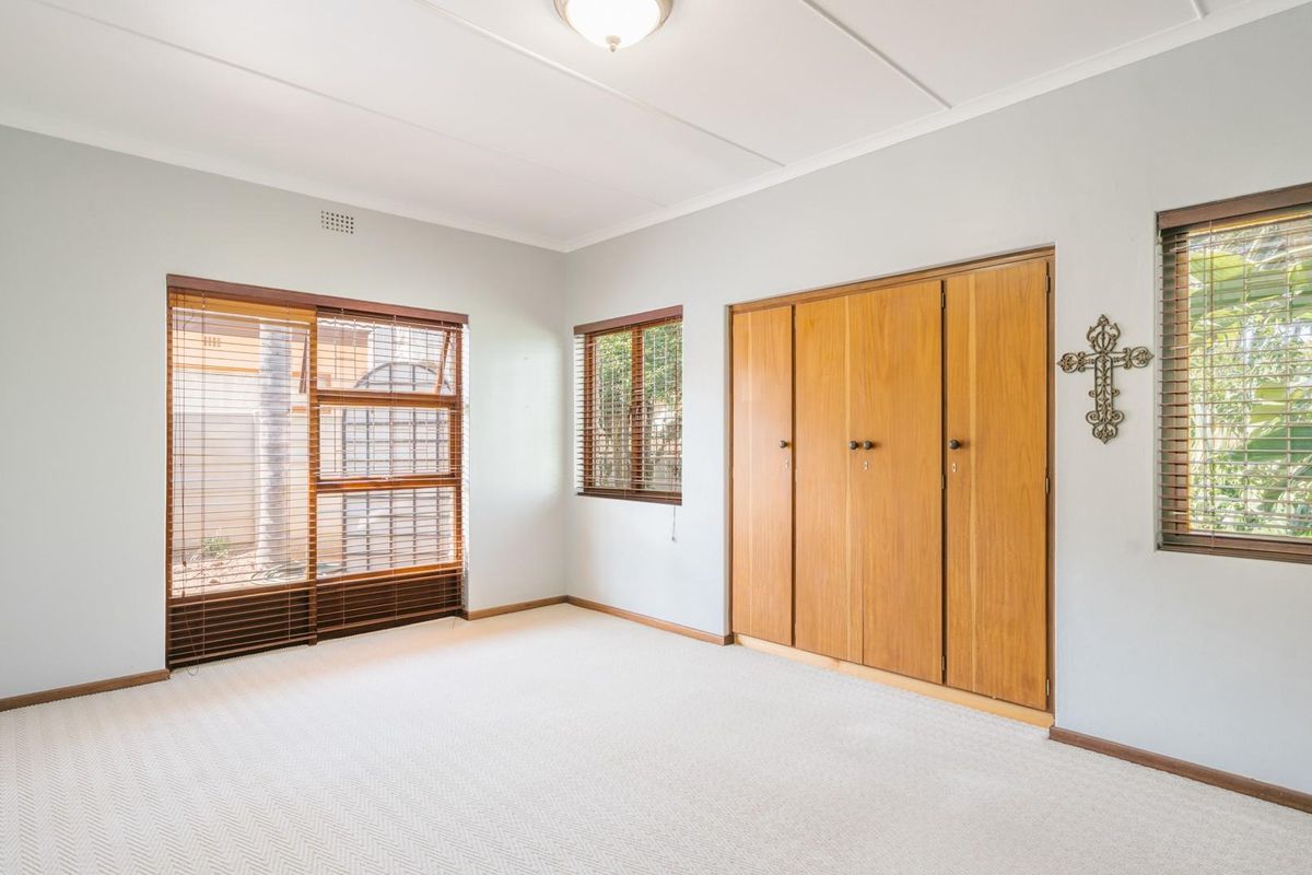 A bright bedroom featuring neutral carpeting, built-in wooden cabinetry, and large windows with fitted blinds, offering a clean and functional living space.