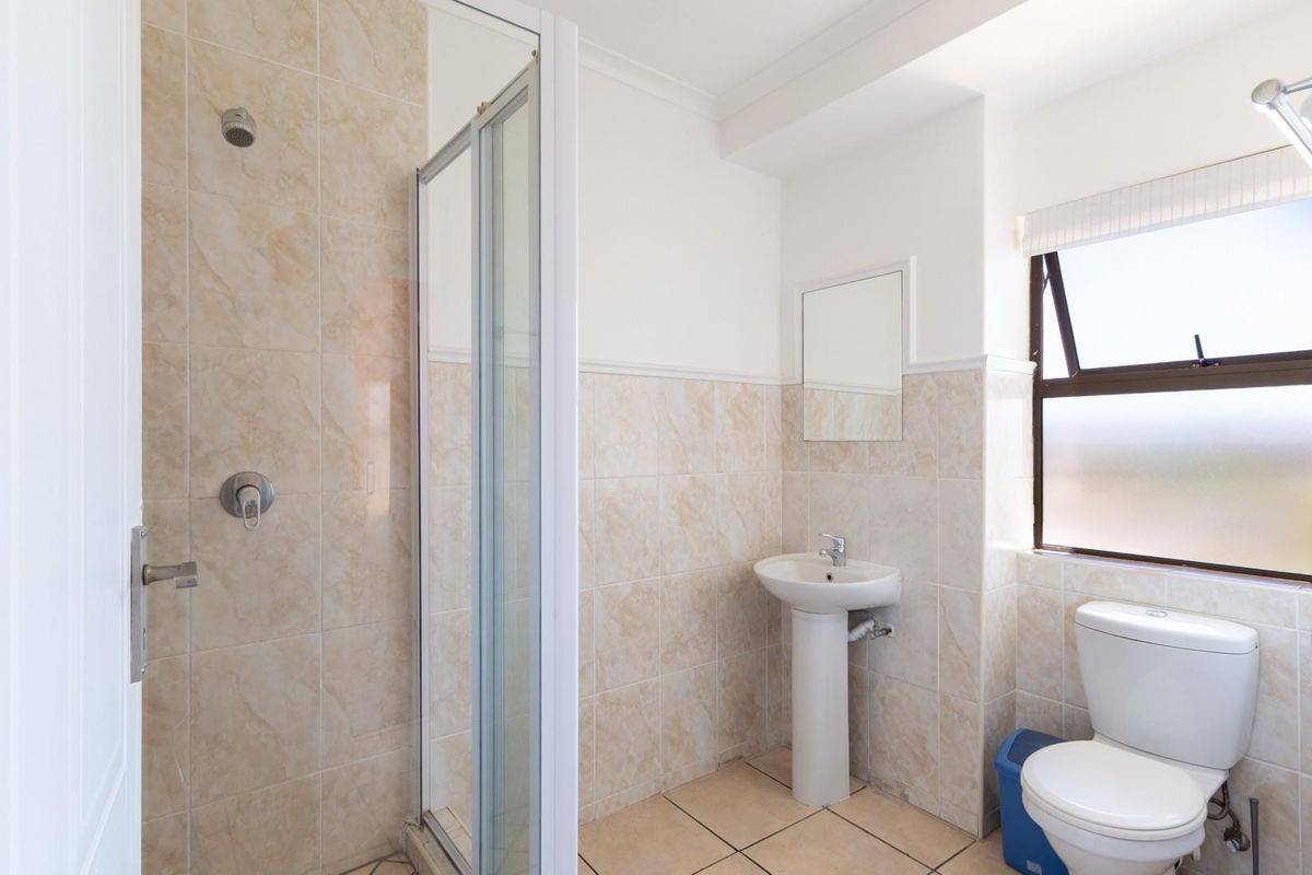A functional bathroom featuring a glass-enclosed shower, a pedestal basin, and a toilet, finished with neutral wall and floor tiling.