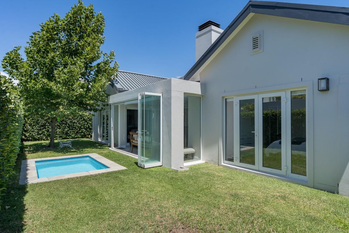 Rear view of the property featuring a manicured lawn, a small plunge pool, and modern glass stacker doors leading into the living area.