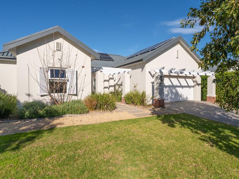 A well-maintained single-story residential home featuring a paved driveway, integrated garage, pergola entrance, and roof-mounted solar panels set within a landscaped garden.