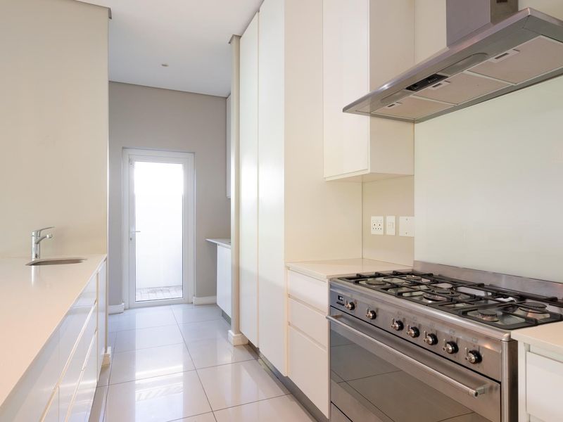Modern kitchen featuring sleek white cabinetry, stone countertops, a gas stove with extractor fan, and tiled flooring with direct access to the exterior.