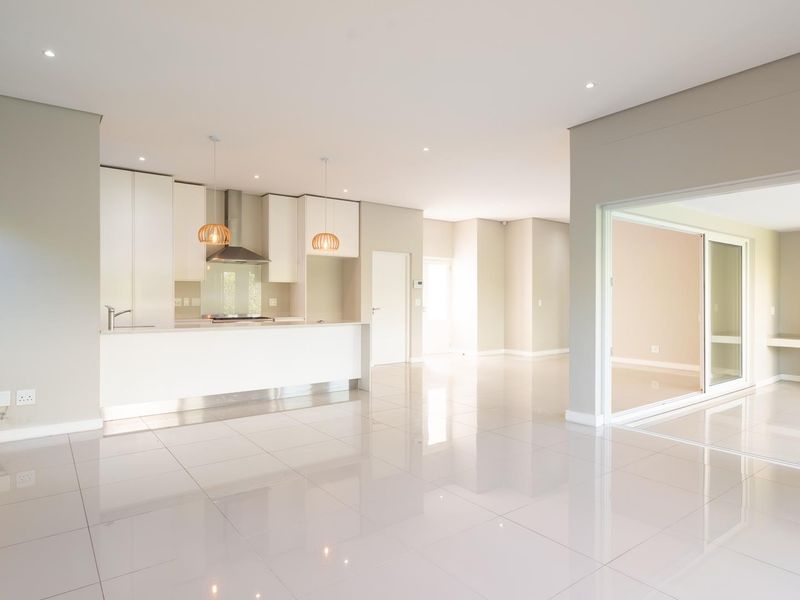 Spacious open-plan living area featuring a modern kitchen with built-in cabinetry, sleek tiled flooring, and seamless access to an adjacent room through sliding doors.