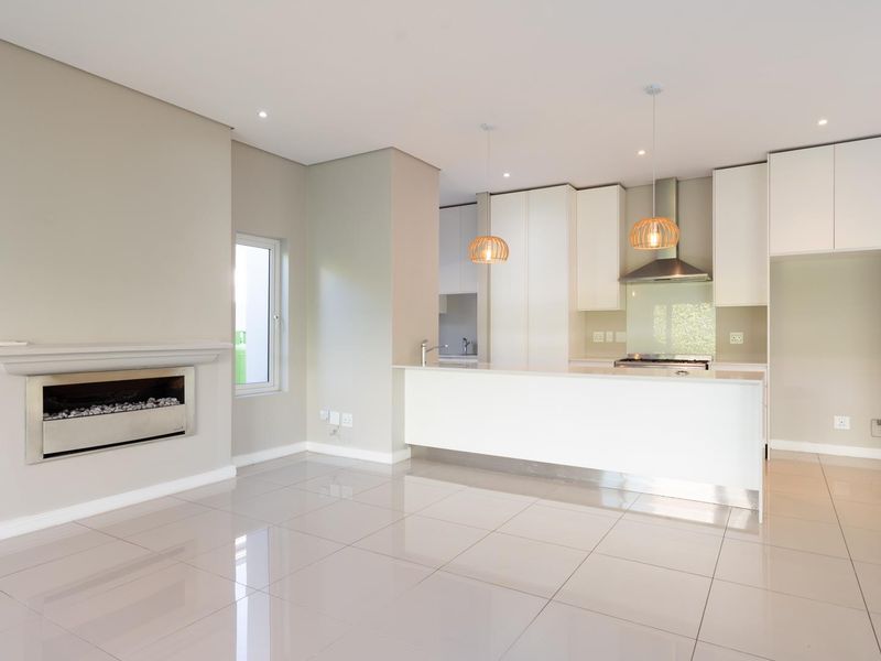 Modern open-plan living area featuring a sleek kitchen with built-in appliances, a central island, and a contemporary fireplace, finished with polished floor tiles.