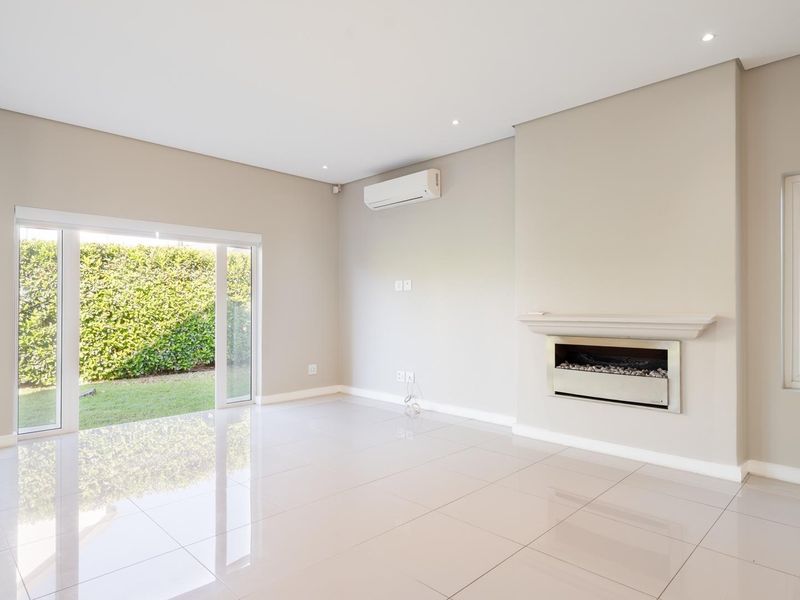 A bright, spacious living area featuring polished tile floors, a modern built-in fireplace, split-system air conditioning, and direct access to the garden.