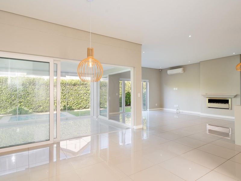 Spacious open-plan living area featuring polished porcelain tiles, a built-in fireplace, split-system air conditioning, and large sliding glass doors leading to the garden.