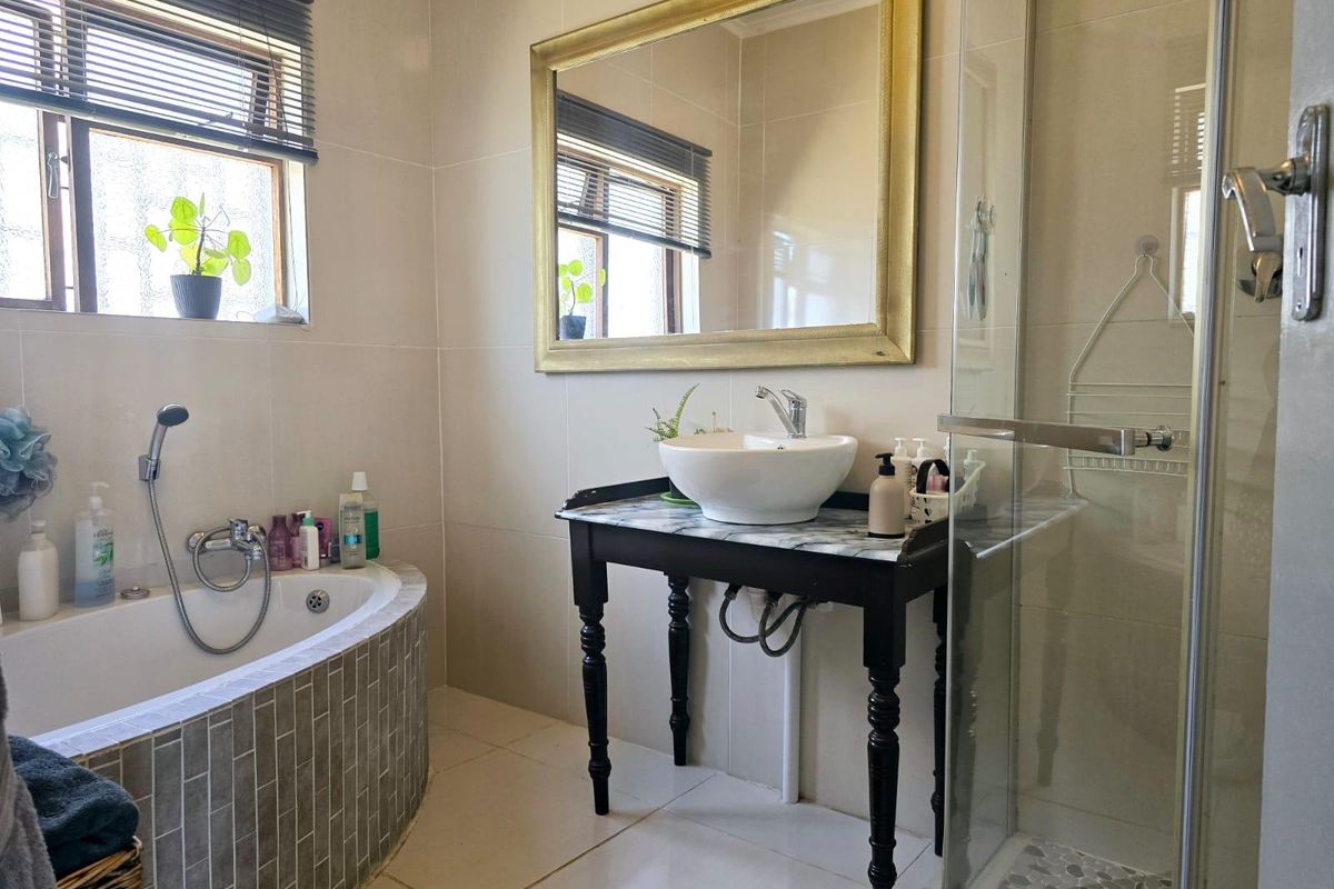 A well-appointed bathroom featuring a curved tiled bathtub, a glass-enclosed shower, and a unique vanity with a vessel sink and marble-style countertop.