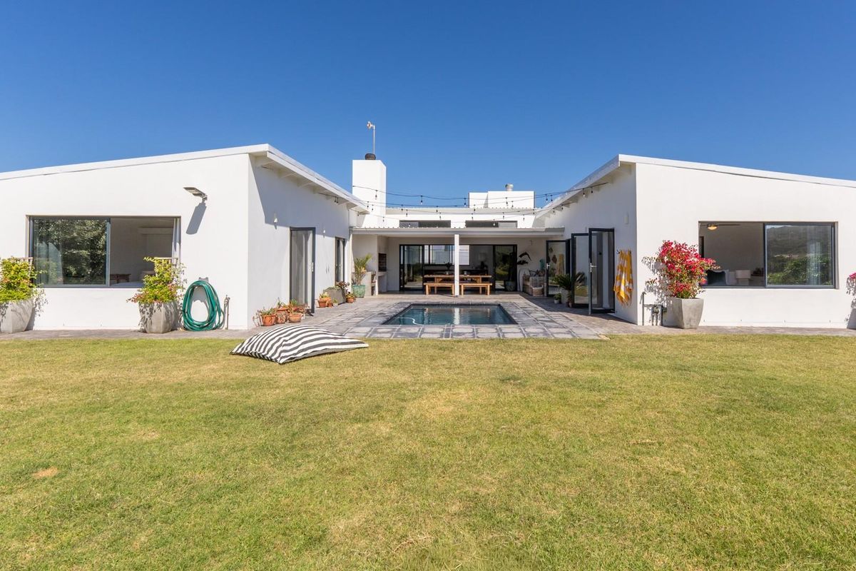 Rear view of a modern white house featuring a central swimming pool, paved patio area, and a spacious lawn.
