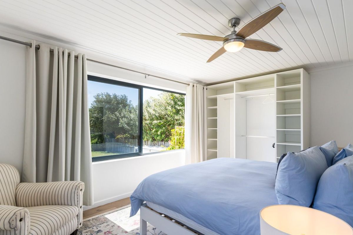 Bright bedroom featuring a large window with garden views, built-in shelving and wardrobe storage, and a modern ceiling fan.