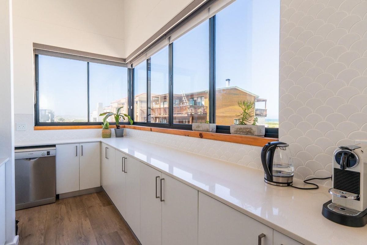 Modern kitchen featuring sleek white cabinetry, stone countertops, integrated dishwasher, and expansive windows offering natural light and scenic views.