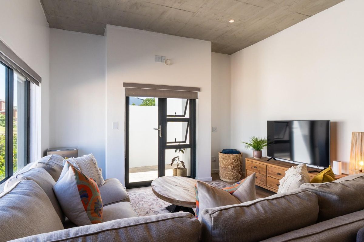 Modern living room featuring an exposed concrete ceiling, large windows, and direct access to an outdoor patio area.