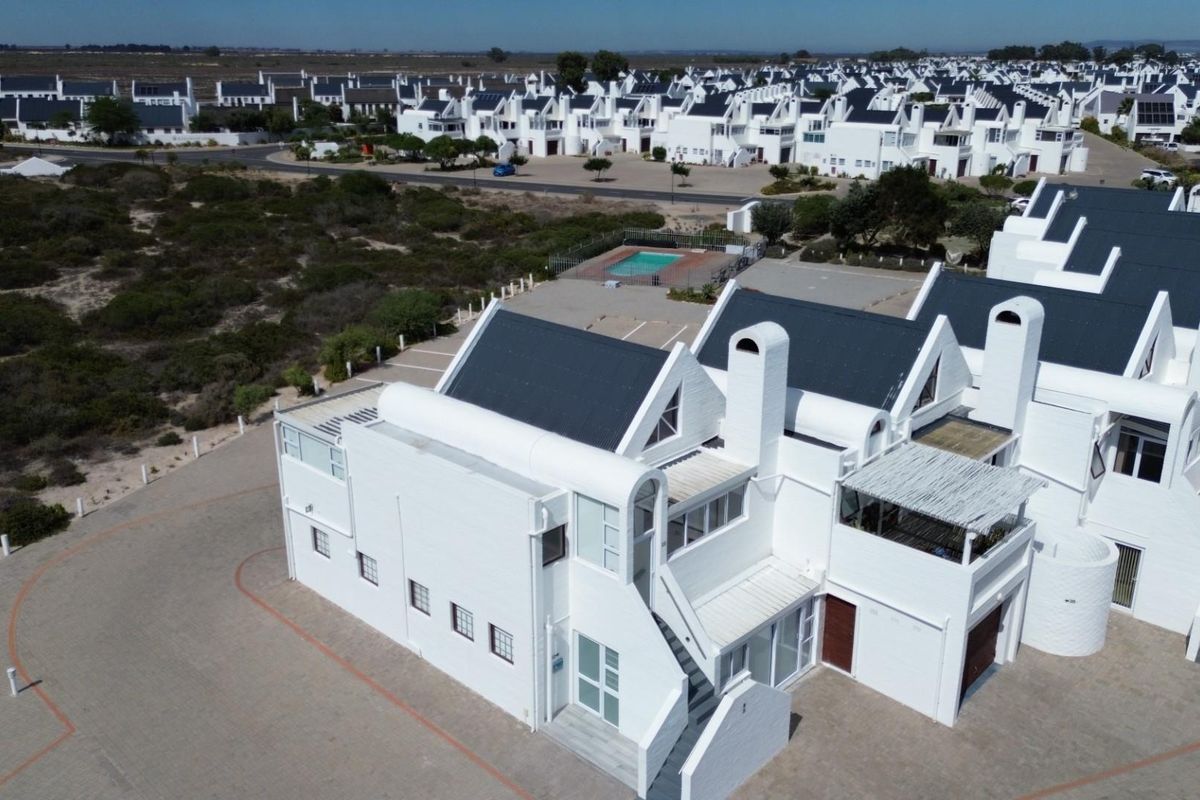 Aerial view of a residential apartment complex featuring white facades, dark pitched roofs, and a communal swimming pool area.