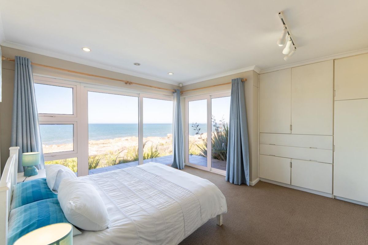 A bright bedroom featuring floor-to-ceiling windows with expansive ocean views, built-in cabinetry, and recessed lighting.