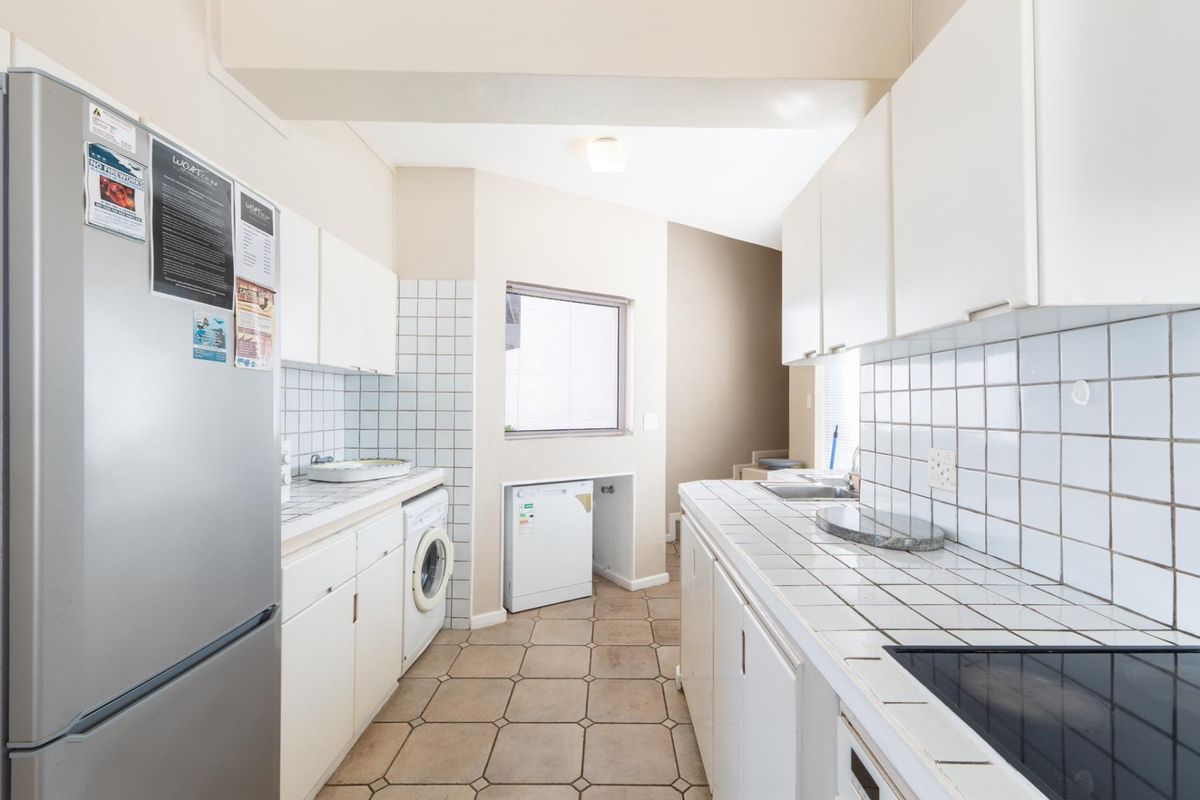 A functional kitchen featuring white cabinetry, tiled countertops, and integrated laundry plumbing, offering a practical layout for daily household tasks.