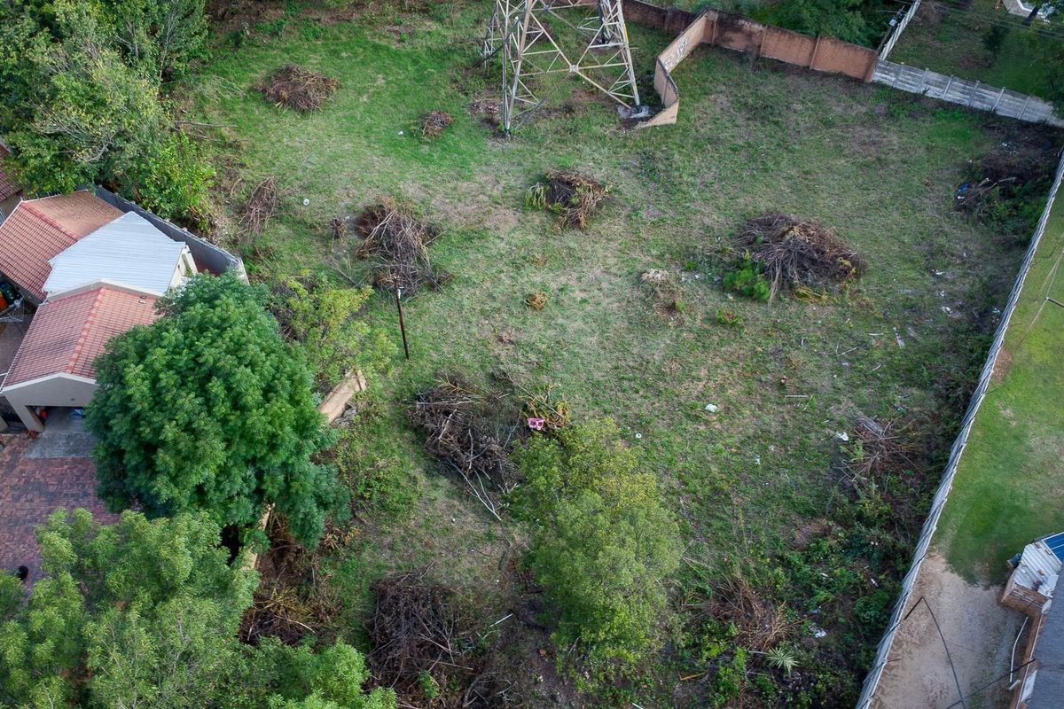 Aerial view of a vacant residential plot featuring established trees, perimeter fencing, and a prominent electrical pylon structure on the property.