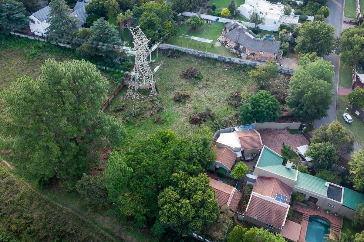 Aerial view of a vacant residential plot featuring mature trees and a prominent high-voltage electricity pylon situated within the property boundaries.