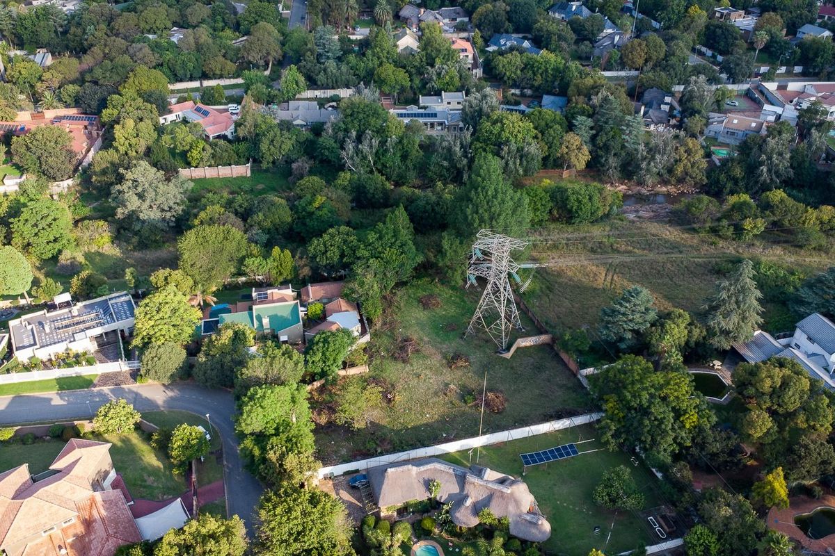 Aerial view of a vacant residential plot featuring mature trees and a prominent electrical pylon situated within a established suburban neighborhood.