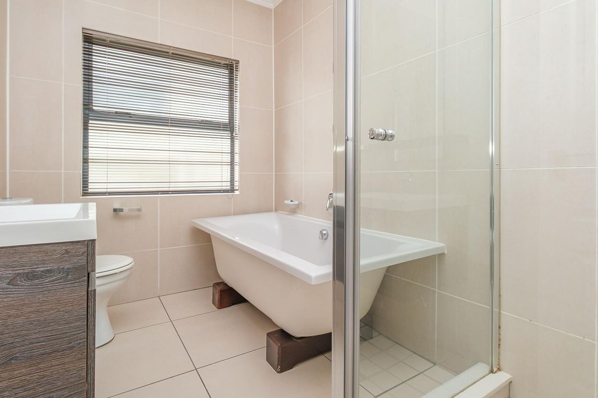 A modern bathroom featuring a freestanding bathtub, a separate glass-enclosed shower, a vanity unit, and neutral wall and floor tiling.
