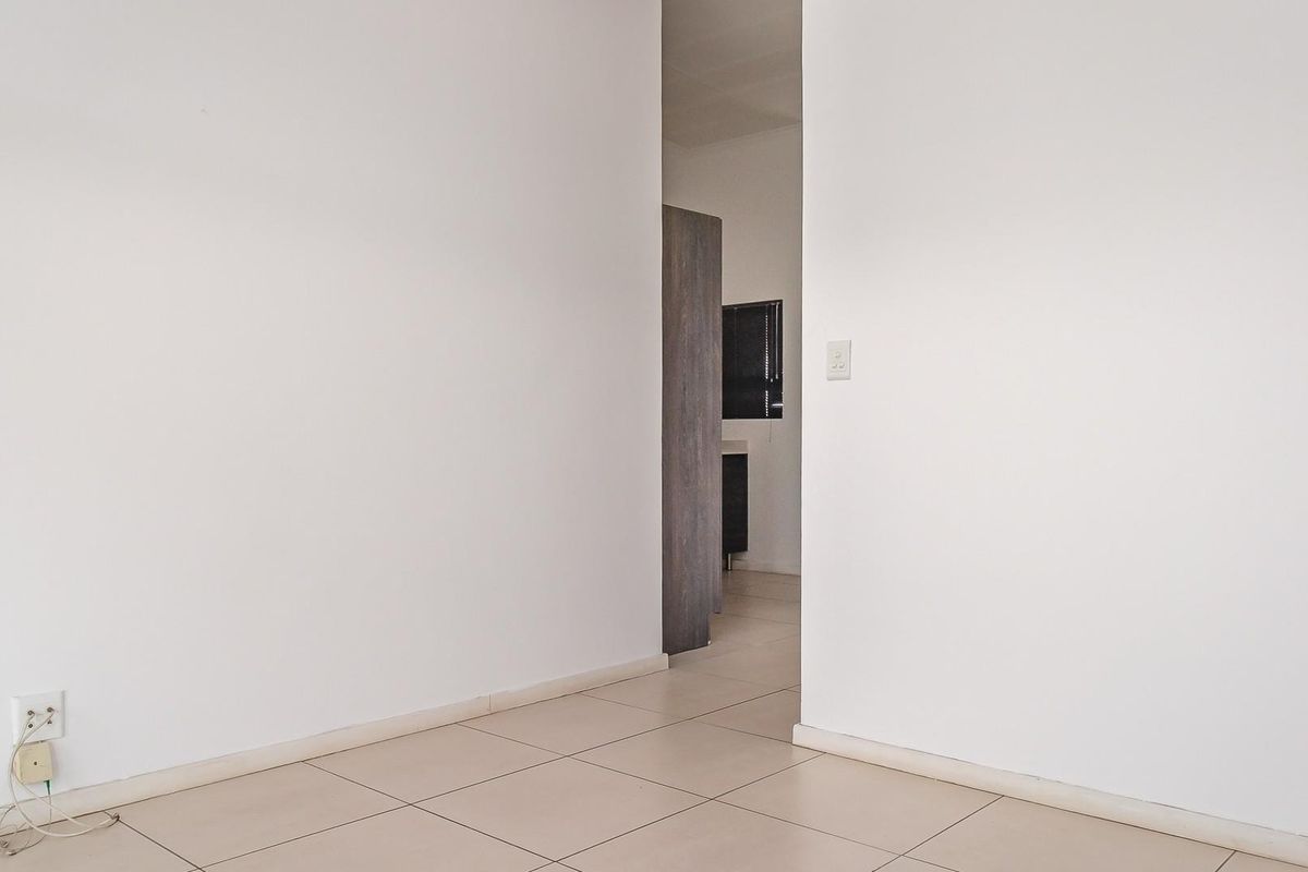 A view from a living area looking through a doorway into an adjacent room, featuring neutral tiled flooring and plain white walls.