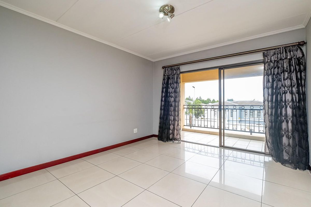 A bright, empty living room featuring large sliding glass doors that open onto a private balcony, finished with neutral floor tiles.