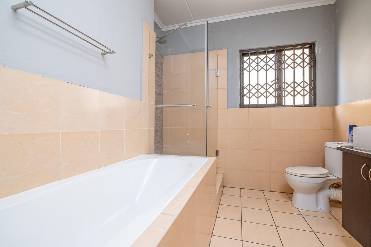 A functional bathroom featuring a built-in bathtub, a glass-enclosed shower, a toilet, and a vanity unit with tiled walls and flooring.
