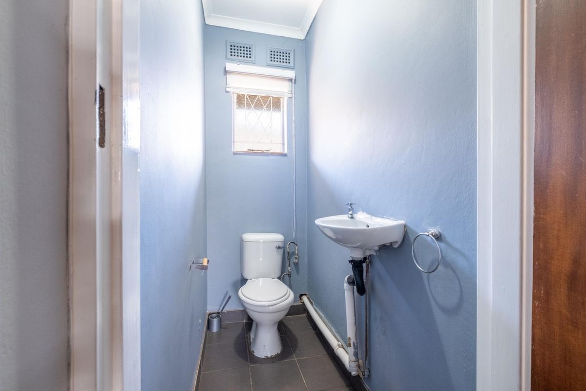 A compact guest bathroom featuring a standard toilet, wall-mounted basin, and tiled flooring.