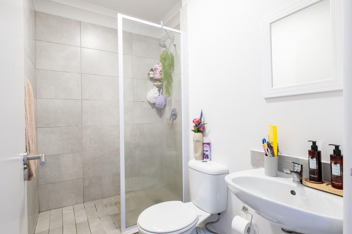 A clean and functional bathroom featuring a walk-in shower with grey tiling, a white pedestal basin, and a standard toilet.