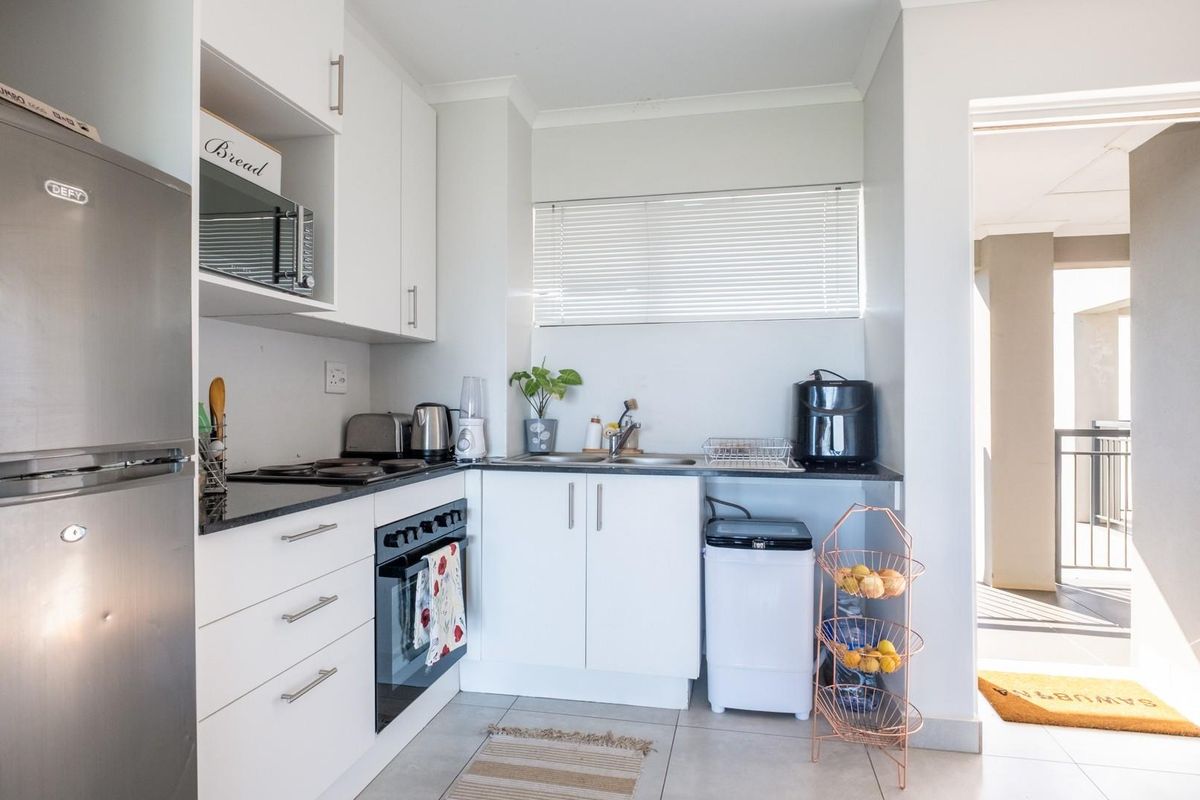 Compact kitchen featuring white cabinetry, dark countertops, built-in oven, and hob, with direct access to an outdoor balcony area.