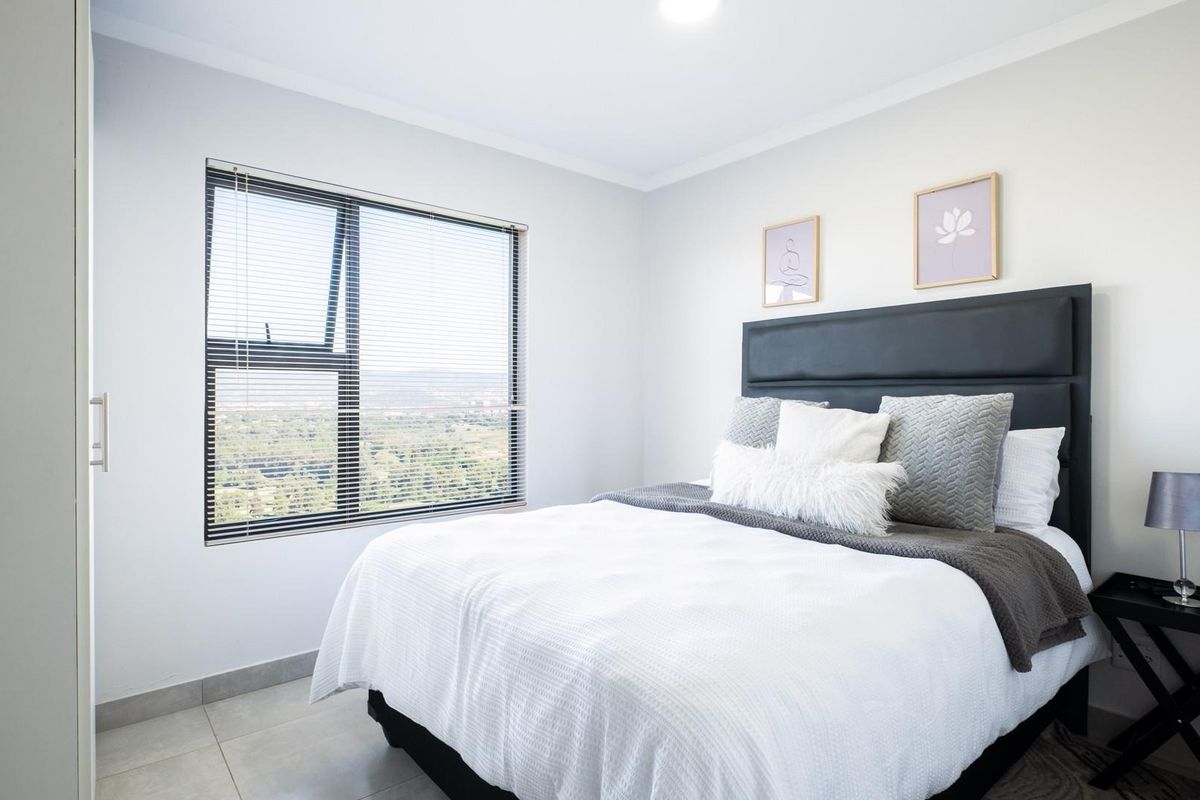 A bright and modern bedroom featuring tiled flooring, a large window with integrated blinds, and a built-in wardrobe.