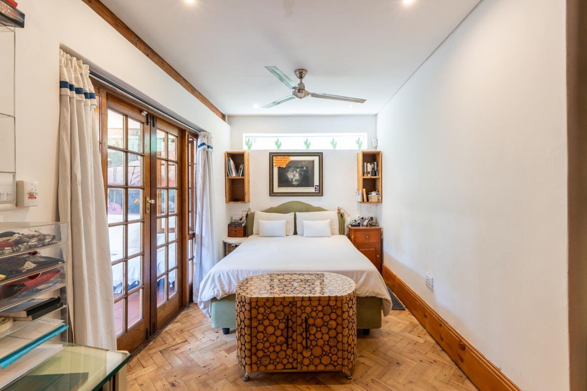 A bedroom featuring parquet timber flooring, a ceiling fan, and wooden French doors providing direct access to the outdoor area.