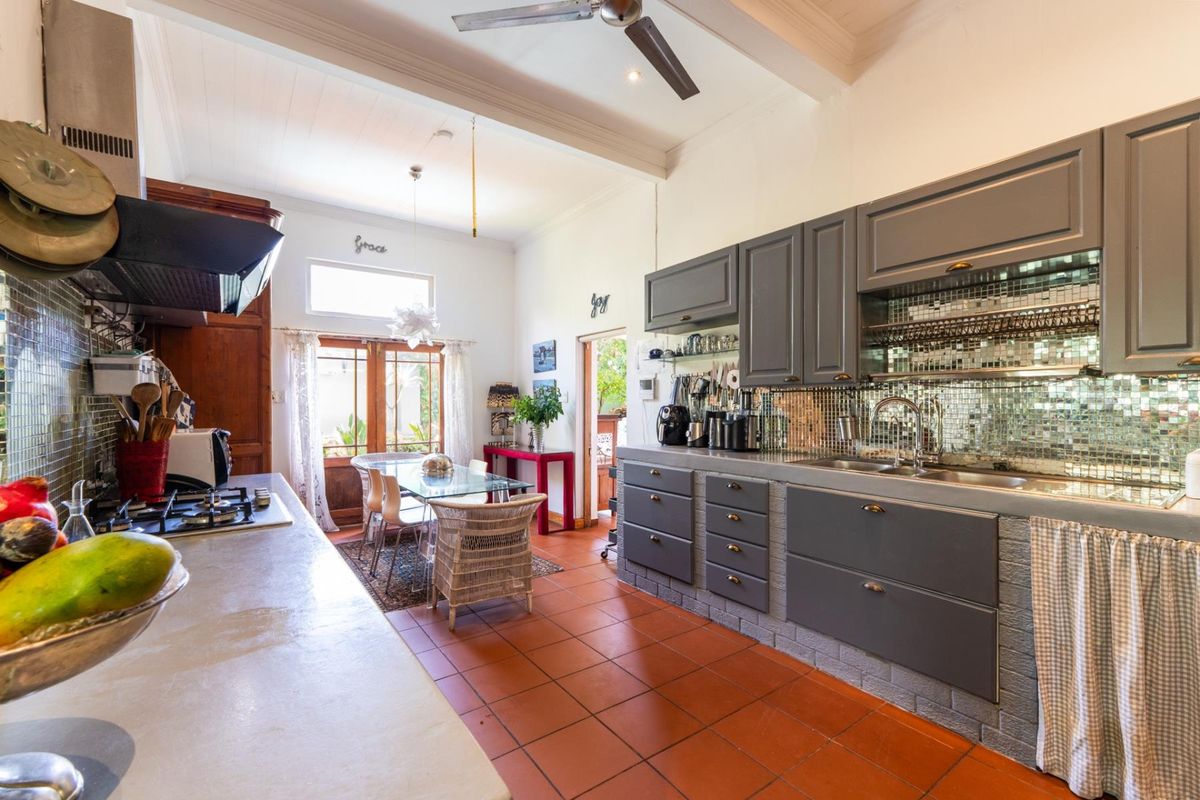 Spacious kitchen featuring grey cabinetry, mosaic tile backsplash, gas hob, extractor fan, and terracotta tile flooring with direct access to the outdoor area.