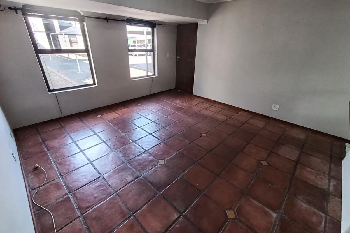 An empty living room featuring terracotta tiled flooring, neutral walls, and aluminium-framed windows, offering a blank canvas for interior design.