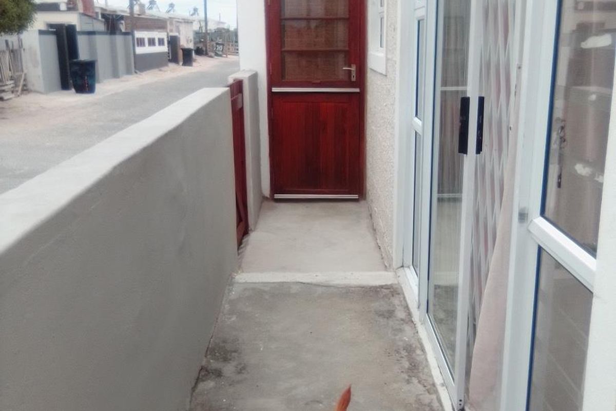 A narrow exterior side passage featuring a solid timber stable-style door, concrete flooring, and sliding glass door access to the main dwelling.